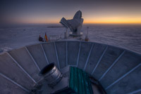 The sun sets behind BICEP2 (in the foreground) and the South Pole Telescope (in the background). (<i>Steffen Richter, Harvard University</i>)